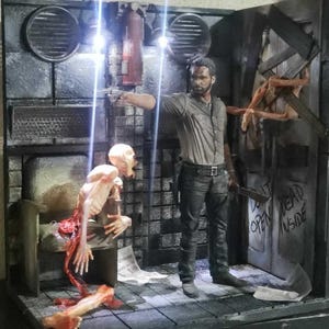 May include: A detailed diorama featuring a figure pointing a gun, a zombie, and a partially open door with the words "DON'T OPEN DEAD INSIDE." The scene is set in a dark, industrial environment with a gray and black color scheme.