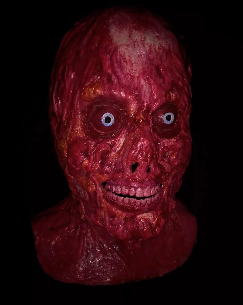 Pu&ograve; includere: Una spaventosa maschera di Halloween, in tonalit&agrave; rosse, raffigurante un volto in decomposizione con carne esposta. La maschera presenta ampie orbite blu, una bocca spalancata che rivela i denti e un aspetto strutturato e invecchiato. La maschera &egrave; ambientata su uno sfondo nero.