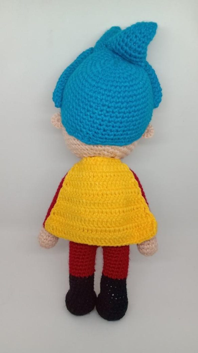 Pu&ograve; includere: Bambola all'uncinetto con capelli blu, viso abbronzato e mantello giallo. La bambola ha braccia e gambe rosse, scarpe nere e piccole orecchie beige. La bambola &egrave; fatta a mano.