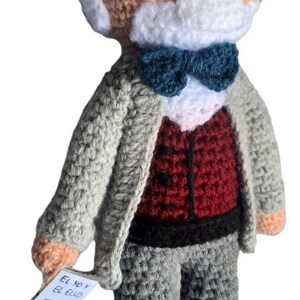 May include: Crocheted doll of a man with glasses, a white beard, and a blue bow tie. He wears a grey suit jacket over a red waistcoat and grey trousers. A small tag reads "El Yo y El Ello Freud."
