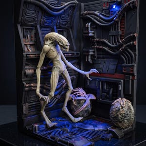 May include: A detailed diorama featuring a pale, slender alien figure with a long head, standing in a futuristic, industrial setting. The scene includes two alien eggs and intricate mechanical details, with blue lighting enhancing the sci-fi aesthetic.
