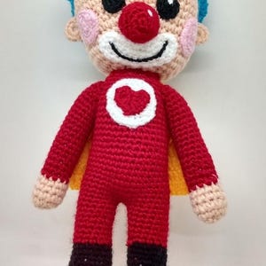 Pu&ograve; includere: Bambola all'uncinetto fatta a mano a forma di supereroe clown. La bambola ha una tuta rossa con un emblema a cuore bianco, capelli blu, naso rosso e stivali neri. Ha un mantello giallo ed &egrave; fatta di filato.