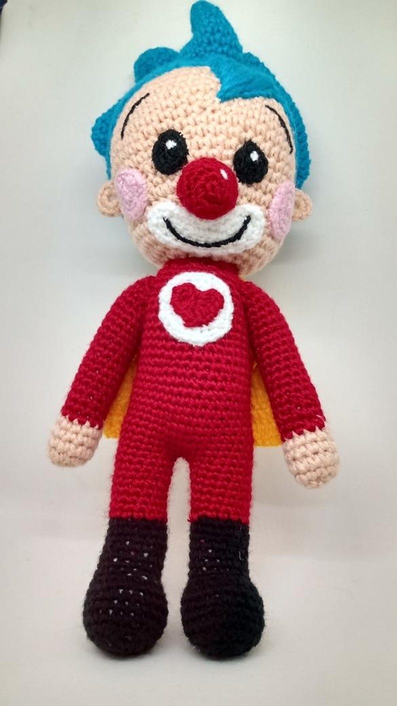 Pu&ograve; includere: Bambola all'uncinetto fatta a mano a forma di supereroe clown. La bambola ha una tuta rossa con un emblema a cuore bianco, capelli blu, naso rosso e stivali neri. Ha un mantello giallo ed &egrave; fatta di filato.