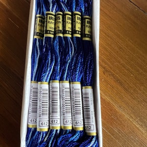 May include: A box of six spools of Iris brand 100% rayon embroidery floss in a blue and white color combination. Each spool is 8 meters long and has a barcode label with the number 7 501120 001128 and 612.