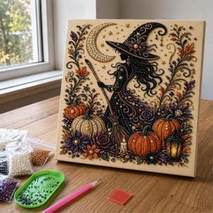 May include: A diamond painting kit featuring a witch in a pointed hat holding a broomstick, surrounded by pumpkins, autumn leaves, and a crescent moon. The artwork is composed of colorful beads on a canvas, accompanied by a green tray and beads.