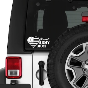 May include: White vinyl decal featuring a heart with the American flag design and the words "Proud Army Mom". The decal is displayed on the rear window of a white vehicle, near the tire.
