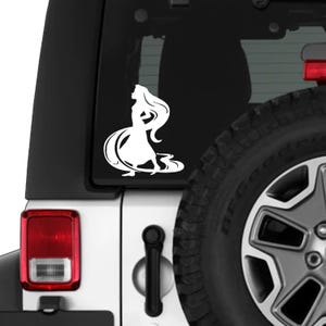 May include: White vinyl decal of a long-haired woman in a flowing dress. The silhouette is applied to the rear window of a vehicle, with the tire and taillight visible in the background. The design is a stylized illustration.