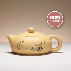 May include: A beige ceramic teapot with a rounded body, a curved handle, and a small spout. The teapot features a lid with a small knob and a black ink drawing of plants. The text "SHIPS FAST" is in a red circle.