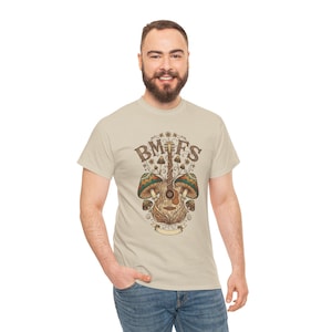 May include: Beige t-shirt featuring a detailed illustration of a guitar with mushrooms and the text "BMFS" in a decorative font. The design incorporates earthy tones of brown, green, and beige, creating a nature-inspired aesthetic.