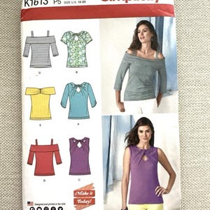May include: A Simplicity sewing pattern envelope labeled K1613, size U.S. 12-20. The front displays illustrations and photographs of various top designs, including off-the-shoulder styles and sleeveless tops with cutout necklines in striped, solid, and patterned fabrics.