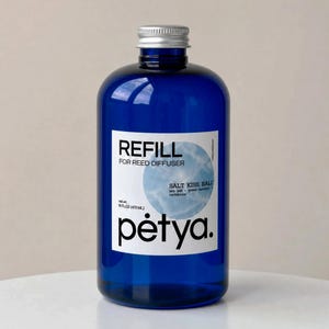 May include: A cobalt blue glass bottle with a silver screw cap containing 16 fl oz of reed diffuser refill. The white label features the text REFILL FOR REED DIFFUSER, SALT KISS, BALI, sea salt, green bamboo, cantaloupe, and the brand name pėtya.
