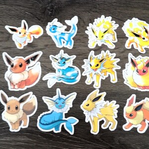 May include: A collection of colorful stickers featuring various Pokémon characters. The stickers showcase Eevee, Vaporeon, Jolteon, and Flareon in different poses. The stickers are white-bordered and appear to be die-cut.