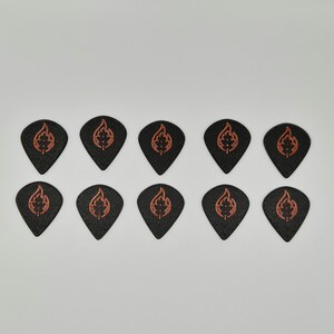 May include: Ten black guitar picks with a flame and leaf design in orange. The picks are arranged in two rows of five against a white background. The picks are made of a textured material.