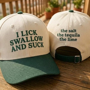 May include: Two baseball caps with a cream-colored crown and a dark green brim. One cap has the text "I LICK SWALLOW AND SUCK" embroidered in green. The other cap has "the salt the tequila the lime" embroidered in green.