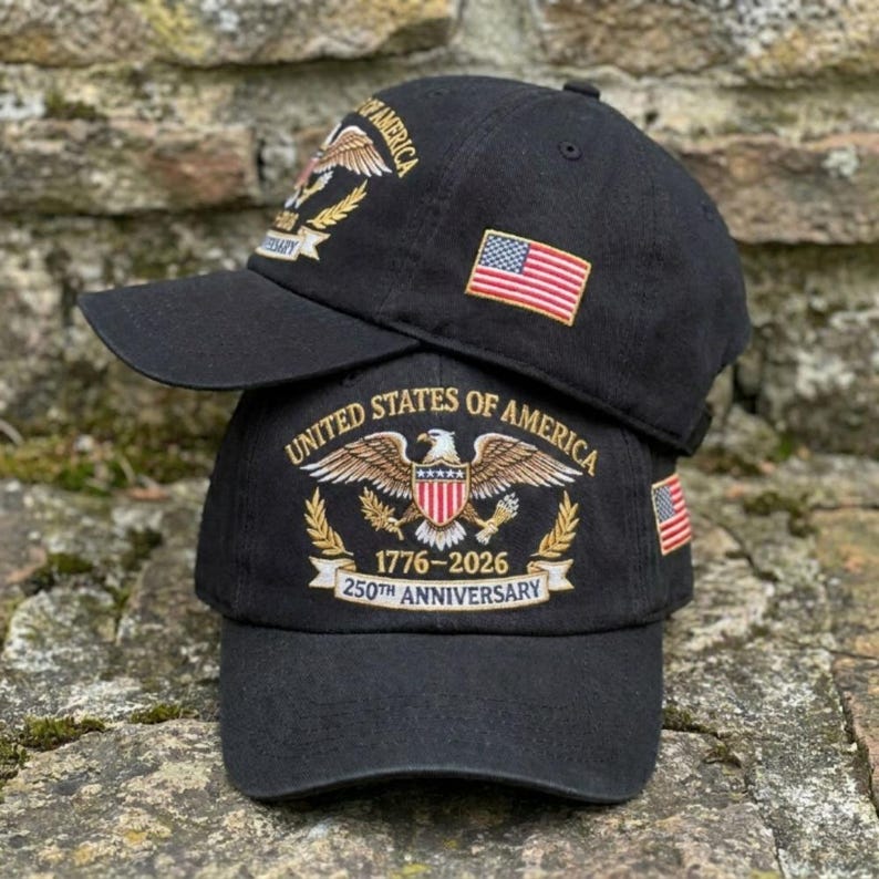 Puede incluir: Dos gorras de b&eacute;isbol negras apiladas una encima de la otra. Cada gorra presenta un dise&ntilde;o bordado con las palabras "United States of America" y un &aacute;guila. Una gorra muestra la bandera estadounidense. La gorra inferior dice "1776-2026 250th Anniversary."