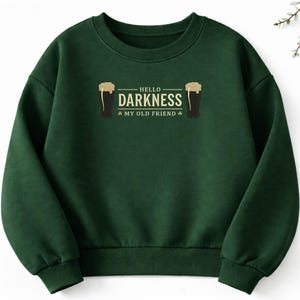 May include: A dark green sweatshirt with the text "HELLO DARKNESS MY OLD FRIEND" in white. The design includes two black beer glasses with foamy tops. The sweatshirt is a crew neck style.