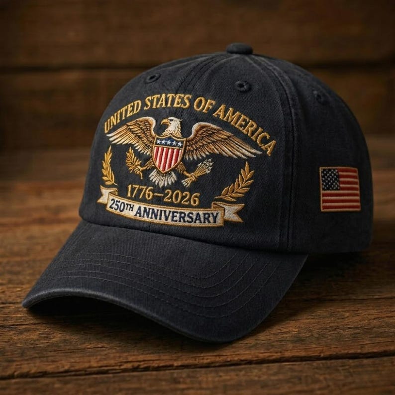 Puede incluir: Gorra de b&eacute;isbol negra con bordados dorados y rojos. La gorra muestra un emblema de &aacute;guila con las palabras "UNITED STATES OF AMERICA" y "1776-2026 250TH ANNIVERSARY". Un parche de la bandera estadounidense est&aacute; en el lateral.