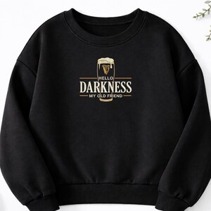 May include: Black sweatshirt with a graphic featuring a pint of beer with the text "HELLO DARKNESS MY OLD FRIEND" in a gold and white design. The sweatshirt is a crew neck style.