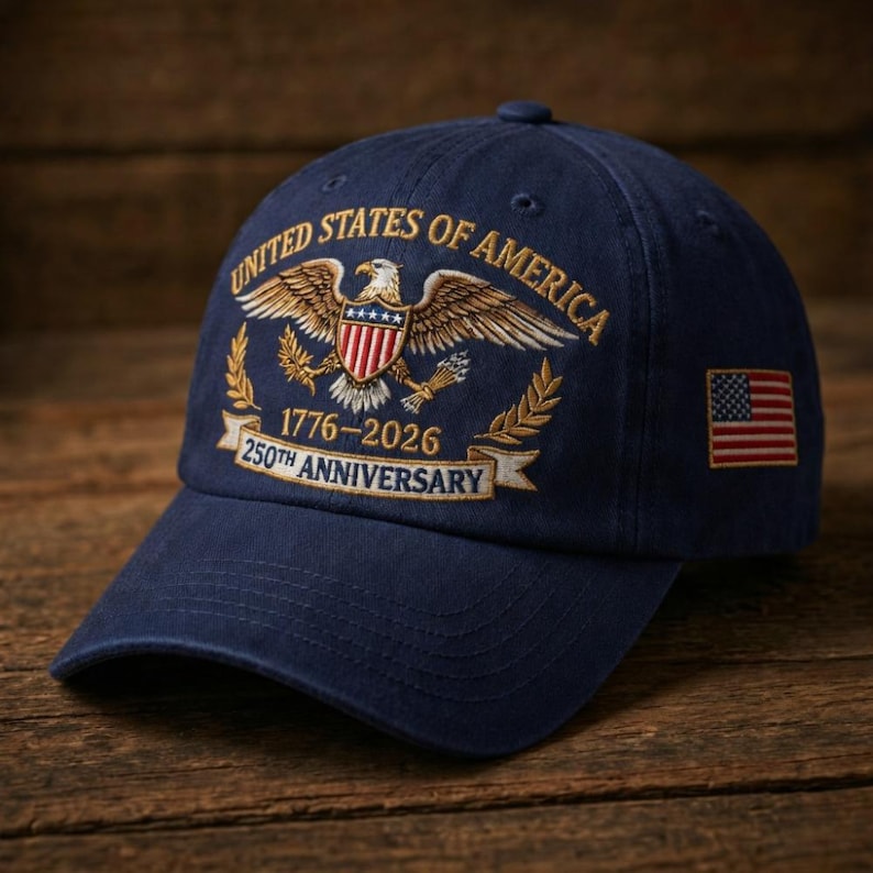 Puede incluir: Gorra de b&eacute;isbol azul marino con detalles bordados. La gorra muestra el texto "UNITED STATES OF AMERICA" sobre un emblema de &aacute;guila, las fechas "1776-2026" y un peque&ntilde;o parche de la bandera estadounidense.