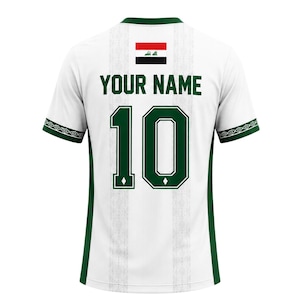 May include: White soccer jersey with green accents, featuring the number 10 and the text "YOUR NAME" in green. The Iraqi flag is displayed above the text. The sleeves have a green and white geometric pattern.