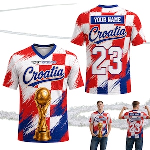 Pu&ograve; includere: Una maglia da calcio della Croazia con un design a scacchi rosso, bianco e blu. La parte anteriore presenta la scritta "Croatia", un trofeo dorato e il testo "Victory Soccer 2026". Il retro mostra il numero 23 e uno spazio per un nome.