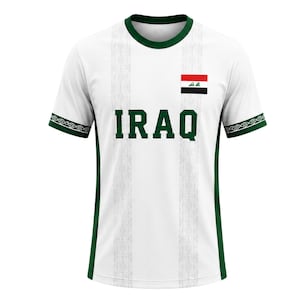 May include: White t-shirt with green accents, featuring the word "IRAQ" in green block letters. The shirt has a green collar and sleeve trim with a geometric pattern. An Iraqi flag is on the upper right chest.