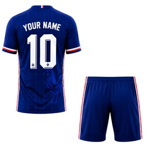Pu&ograve; includere: Un completo da calcio blu composto da maglia e pantaloncini. La maglia presenta il numero 10 in bianco, con la scritta "YOUR NAME" sopra. Accenti rossi e bianchi adornano le maniche e il colletto. I pantaloncini sono blu con strisce rosse e bianche sui lati.