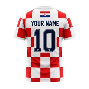May include: A white and red checkered soccer jersey with the Croatian flag at the top. The jersey has the number 10 in navy blue and the text "YOUR NAME" above it. The jersey is short-sleeved.