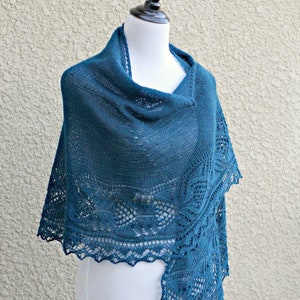 May include: A teal blue knitted shawl with a delicate lace pattern. The shawl is draped over a white mannequin.