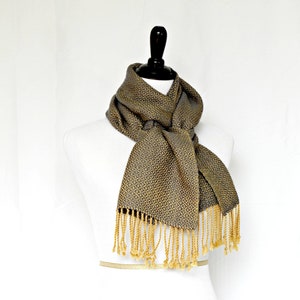 May include: A gray and gold patterned scarf with gold fringe. The scarf is tied around a white mannequin.
