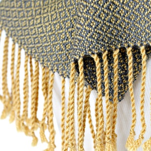 May include: A gray and yellow woven scarf with a geometric pattern and yellow fringe.