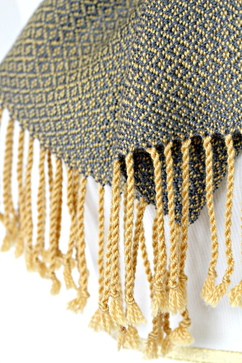 May include: A gray and yellow woven scarf with a geometric pattern and yellow fringe.