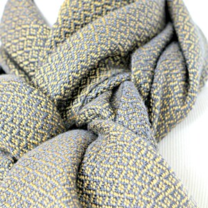 May include: A gray and yellow woven scarf with a geometric pattern. The scarf is folded and draped over a mannequin.