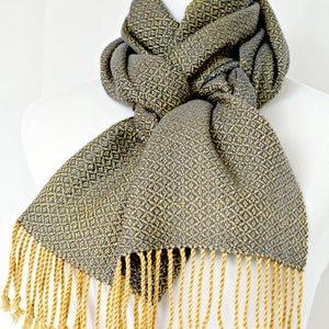May include: A gray and yellow woven scarf with a diamond pattern and yellow fringe.