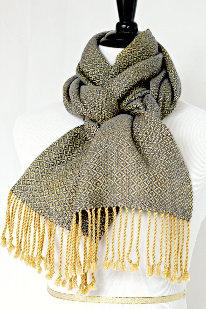 May include: A gray and yellow woven scarf with a diamond pattern and yellow fringe.