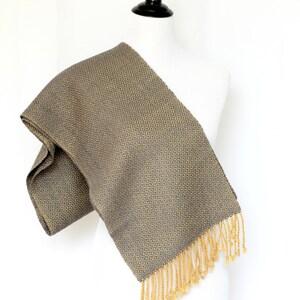 May include: A gray and gold woven scarf with a geometric pattern and gold fringe.