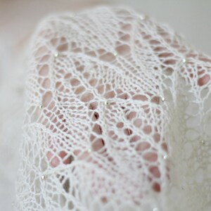 May include: A white crocheted shawl with a delicate lace pattern and small silver beads.