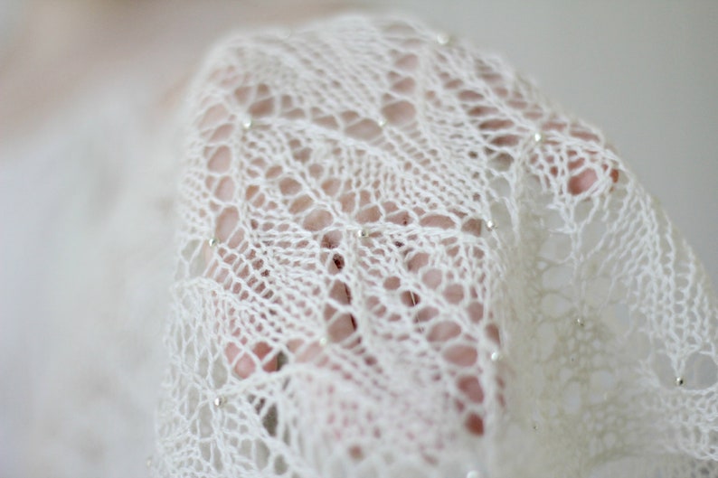 May include: A white crocheted shawl with a delicate lace pattern and small silver beads.