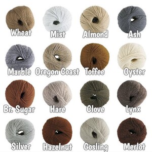 May include: A colour chart of yarn samples in various shades of brown, grey, beige, and white. The yarn is arranged in a grid with labels below each sample, including "Wheat", "Mist", "Almond", "Ash", "Marble", "Oregon Coast", "Toffee", "Oyster", "Br. Sugar", "Hare", "Clove", "Lynx", "Silver", "Hazelnut", "Gosling", and "Merlot".