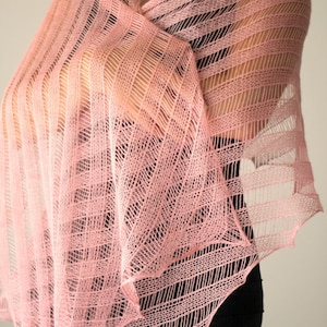 May include: A delicate pink knitted shawl with a lacy pattern. The shawl is draped over a person's shoulders and is made of a lightweight, airy fabric.