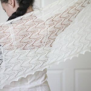 May include: A white lace shawl with a delicate pattern. The shawl is draped over a person's shoulders and is made of a soft, lightweight fabric.