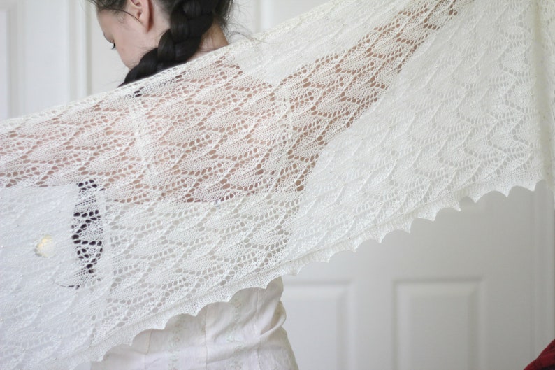 May include: A white lace shawl with a delicate pattern. The shawl is draped over a person's shoulders and is made of a soft, lightweight fabric.