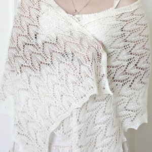 May include: A white crocheted shawl with a delicate lace pattern. The shawl is draped over a person's shoulders and is worn with a white dress.