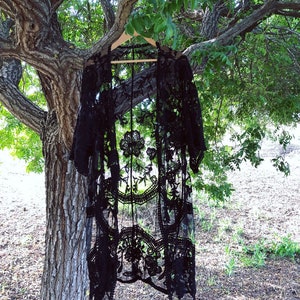 May include: Black lace kimono hanging from a tree branch. The kimono has a delicate floral pattern and a flowing silhouette.