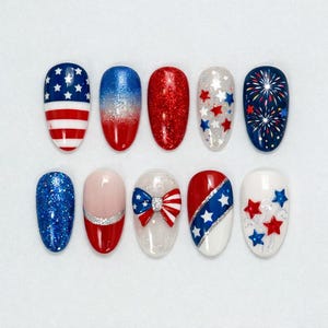 May include: A collection of ten nail designs featuring patriotic themes. Designs include red, white, and blue colors, glitter, stars, stripes, and a bow. The nail shapes are oval and the designs are applied on a white background.
