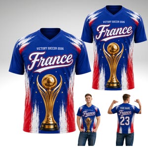 May include: Blue soccer jersey with the word "France" in white script, a gold trophy, and the text "Victory Soccer 2026." The jersey has red and white brushstroke accents and a V-neck.
