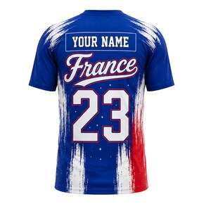 May include: Blue jersey with the word "France" in white script and the number "23" in white. The jersey has a blue and white brushstroke design with red accents. The text "YOUR NAME" is above the word "France".