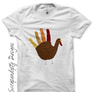May include: White t-shirt with a handprint turkey design. The turkey is made of different colored fabric scraps and has a red wattle and beak.