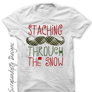 May include: White t-shirt with the text "STACHING THROUGH THE SNOW" in red and green lettering. A plaid green and red mustache is above the text.