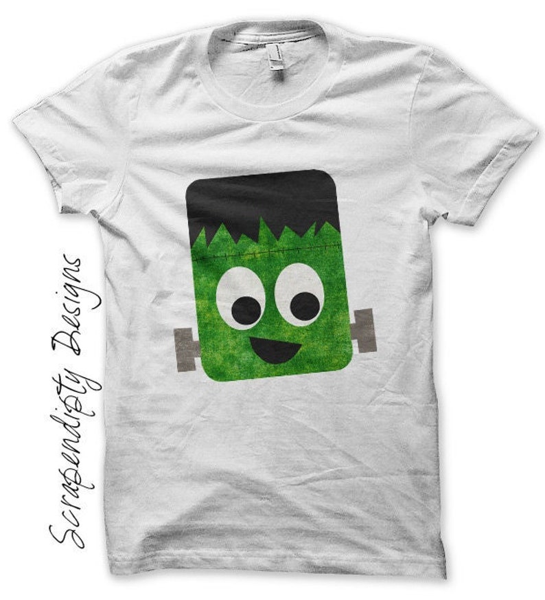Pu&ograve; includere: Maglietta bianca con un grafico di un mostro di Frankenstein verde e nero in stile cartone animato. Il mostro ha occhi grandi e un ampio sorriso.
